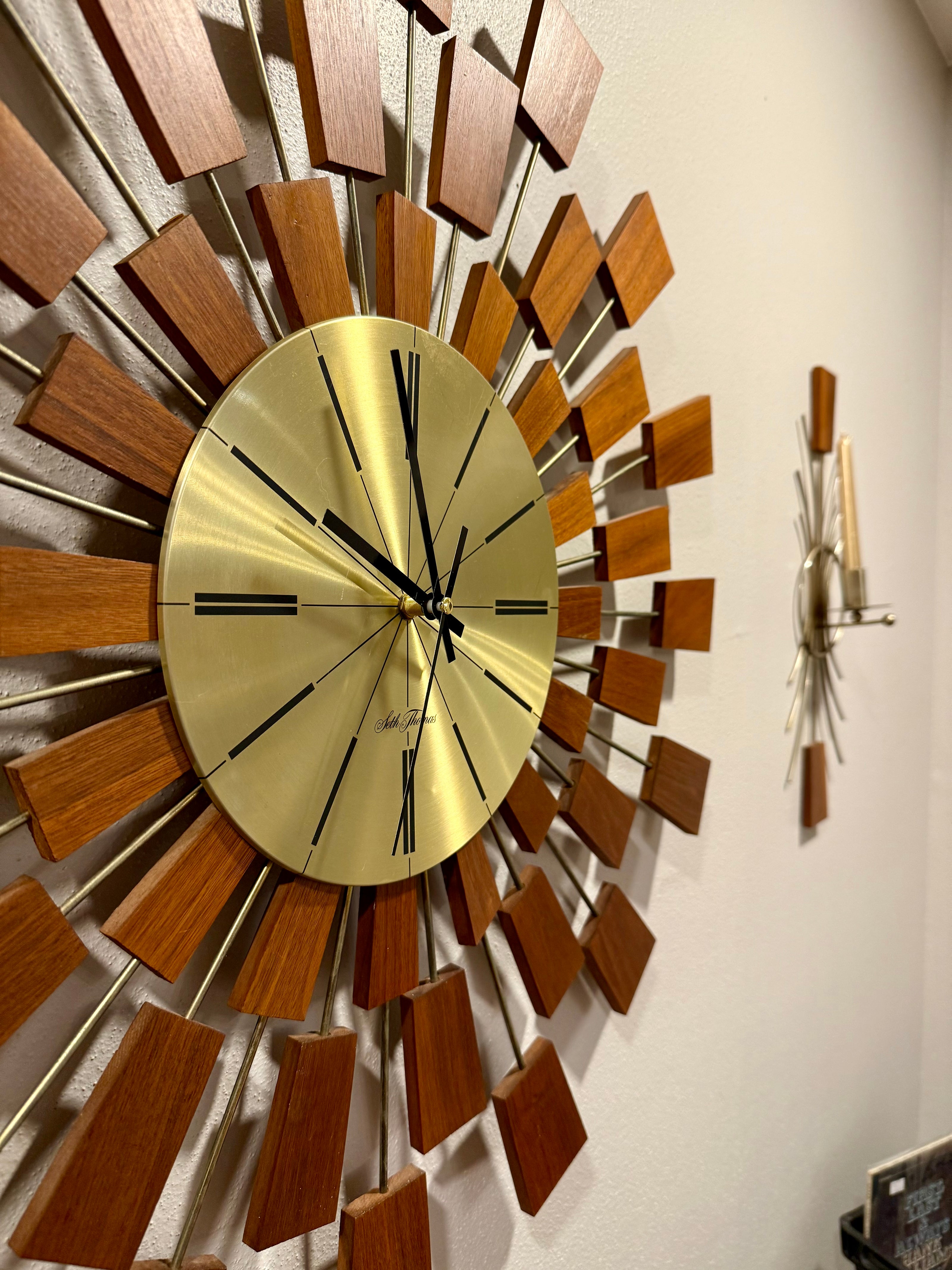 MCM wall clock with wooden and brass design on a white wall.